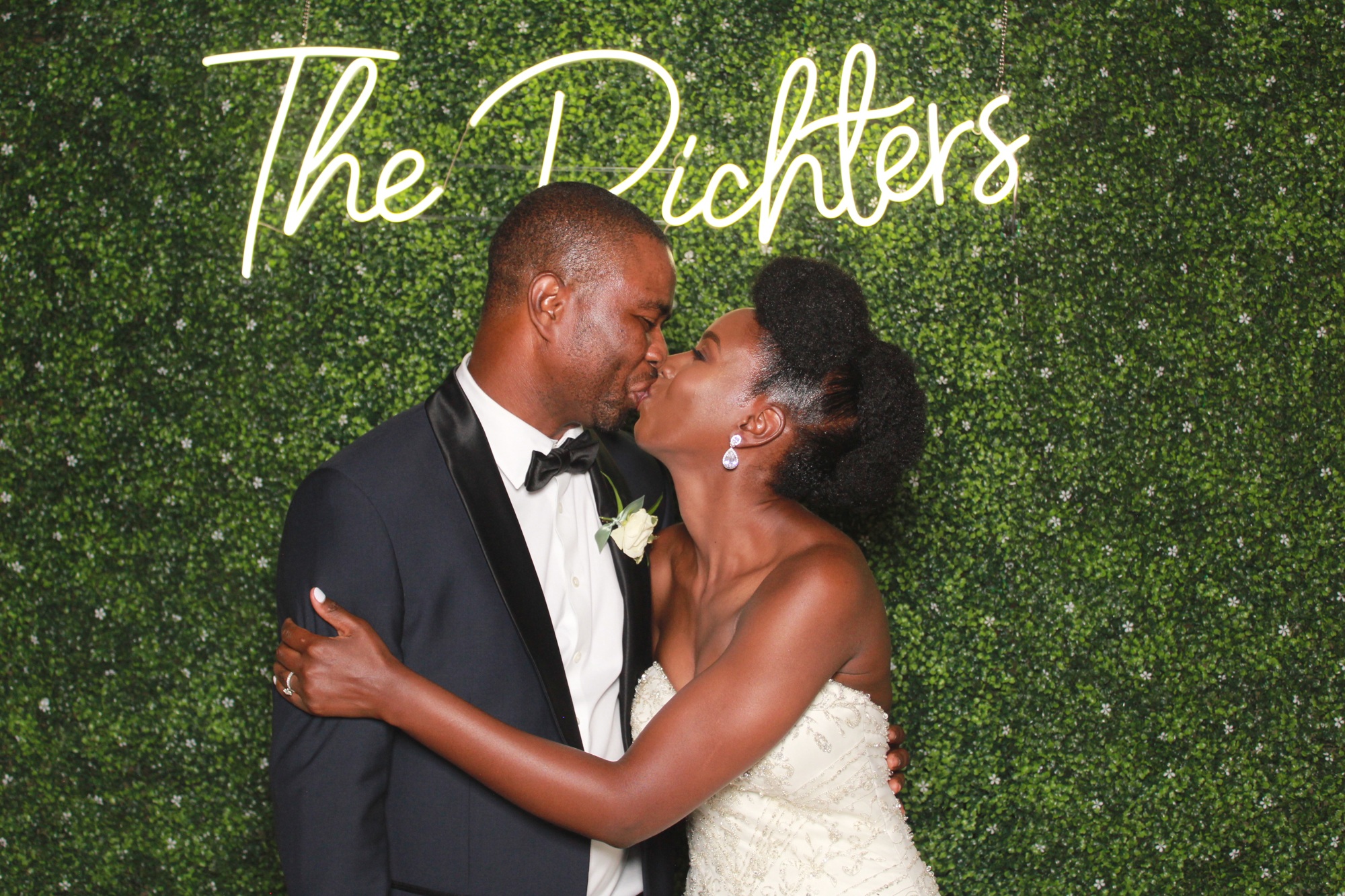 Candace and Emmanuel kissing at their wedding in front of the hedge backdrop
